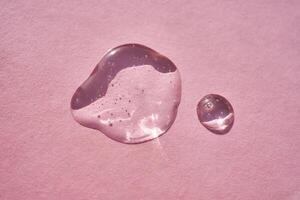 Drop of serum shimmering in the sun on a pink background. photo