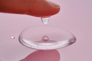 A finger touches a drop of cosmetic product on a pink background. photo
