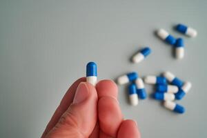 A hand holds a white and blue pill on a blue background. photo