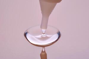 A drop of cosmetic product pours from a tube onto a pink background. photo