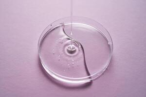 Serum or cosmetic oil flows into a transparent bowl on a purple background. photo