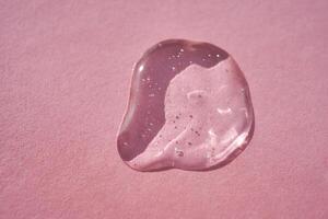 Drop of serum shimmering in the sun on a pink background. photo