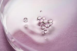 Serum or cosmetic oil flows into a transparent bowl on a purple background. photo