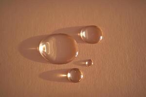 Beautiful volumetric drops of cosmetic product on a beige background. photo