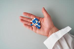 A hand holds a handful of white and blue pills on a blue background. photo