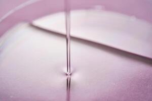 Serum or cosmetic oil flows into a transparent bowl on a purple background. photo