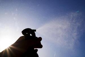 A woman's hand sprays an air freshener against the sky. photo
