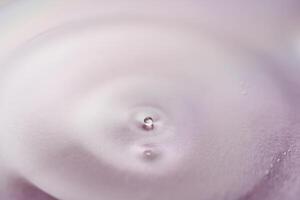 suero o cosmético petróleo fluye dentro un transparente cuenco en un púrpura antecedentes. foto