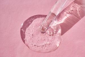 Pipette with serum shimmering in the sun on a pink background. photo