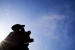 A woman's hand sprays an air freshener against the sky. photo