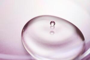 Serum or cosmetic oil flows into a transparent bowl on a purple background. photo