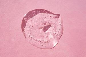 Drop of serum shimmering in the sun on a pink background. photo