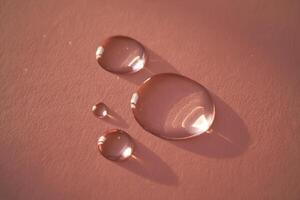 Beautiful volumetric drops of cosmetic product on a pink background. photo