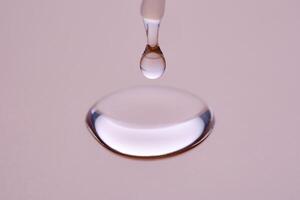 A drop of cosmetic product pours from a tube onto a pink background. photo