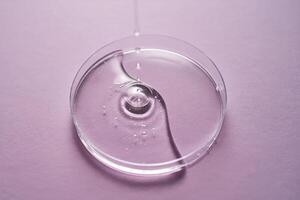 Serum or cosmetic oil flows into a transparent bowl on a purple background. photo