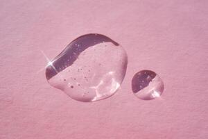 Drop of serum shimmering in the sun on a pink background. photo