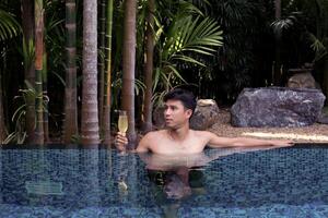 un hombre tiene un descanso en el piscina y disfrutando vaso de sabroso frío blanco vino durante vacaciones. viaje vacaciones. verano vacaciones. foto