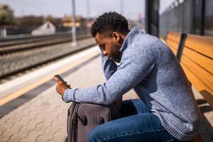 Angry man with a suitcase and mobile phone sitting on a bench at the railway station. photo