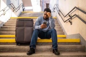 Worried man with a phone and suitcase sitting on a stairs at the railway station photo