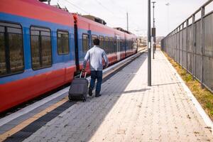 Man running to a leaving train along railway station with suitcase. photo