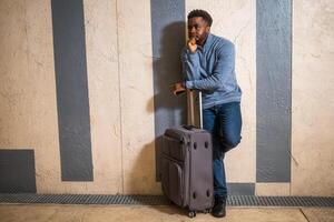 Worried man with suitcase and mobile phone leaning against a wall in passage of the railway station. Copy space on image for your advert or text. photo