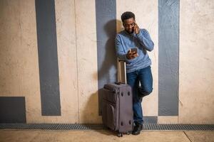 Worried man with suitcase and mobile phone leaning against a wall in passage of the railway station. Copy space on image for your advert or text. photo