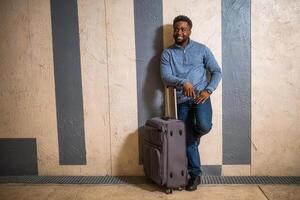 Happy man with suitcase using phone while leaning against a wall in passage of the railway station. Copy space on image for your advert or text. photo