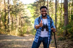 joven hombre disfruta excursionismo en naturaleza y demostración pulgar arriba foto