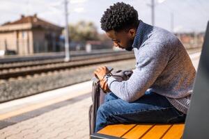 orried man looking at his clock while sitting on a bench at the railway station photo