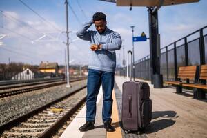 Worried man looking at his clock while standing with suitcase on a railway station. photo