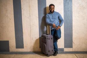 Happy man with suitcase using phone while leaning against a wall in passage of the railway station. Copy space on image for your advert or text. photo