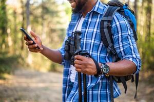 joven hombre disfruta excursionismo y utilizando móvil teléfono en naturaleza foto