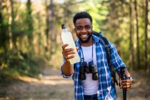 joven hombre disfruta excursionismo y Bebiendo energía beber. atención en botella. foto