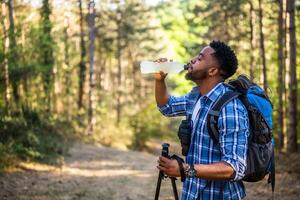 joven hombre disfruta excursionismo y Bebiendo energía beber. foto