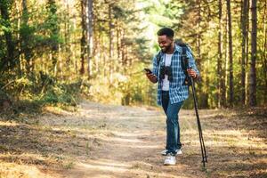 joven hombre disfruta excursionismo y utilizando móvil teléfono en naturaleza. foto