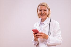 Portrait of mature female doctor using mobile phone on gray background. photo