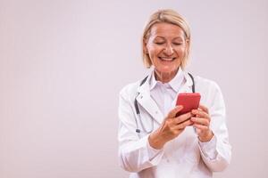 Portrait of mature female doctor using mobile phone on gray background. photo