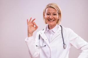 Portrait of mature female doctor showing ok sign on gray background. photo