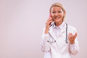 Portrait of mature female doctor using mobile phone on gray background. photo