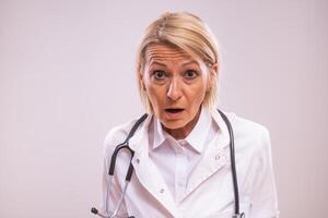 Portrait of shocked mature female doctor on gray background. photo