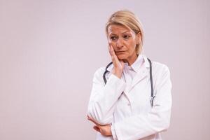 Portrait of tired mature female doctor on gray background photo