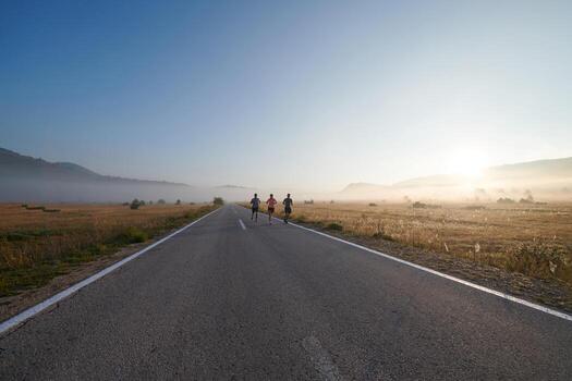 A group of friends, athletes, and joggers embrace the early morning hours as they run through the misty dawn, energized by the rising sun and surrounded by the tranquil beauty of nature photo