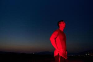 atleta huelgas un actitud debajo rojo Noche resplandor después intenso todo el día maratón. foto