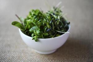 Green salad in a cup on a burlap cloth. Herbal salad on a yellow background. photo