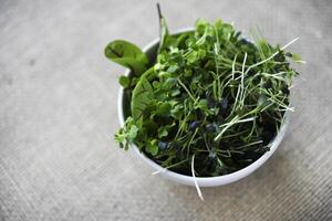 Green salad in a cup on a burlap cloth. Herbal salad on a yellow background. photo