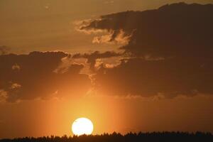 Colorful sunset in the evening. The setting disk of the sun over the forest. Clouds and a yellow sunset. photo