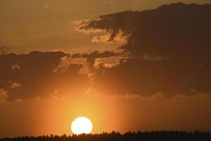 Colorful sunset in the evening. The setting disk of the sun over the forest. Clouds and a yellow sunset. photo