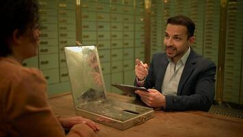 A man and woman are seen sitting at a table in different locations, including a bank and a room with lockers, looking at their phones and conversing. The captures interactions in various video