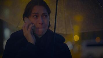 triste donna parlando su cellula Telefono al di fuori a notte nel pioggia tempo metereologico video