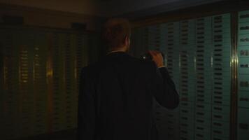 hombre en traje espías investigando bóveda seguro participación un Linterna en oscuro habitación video